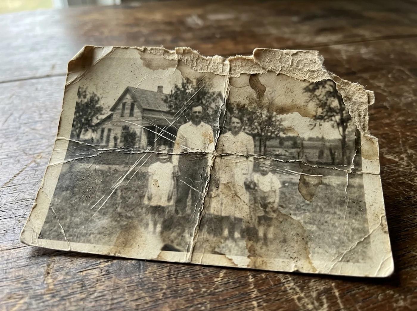 A close-up of an old photo with deep scratches, creases, water stains, and faded areas across a portrait